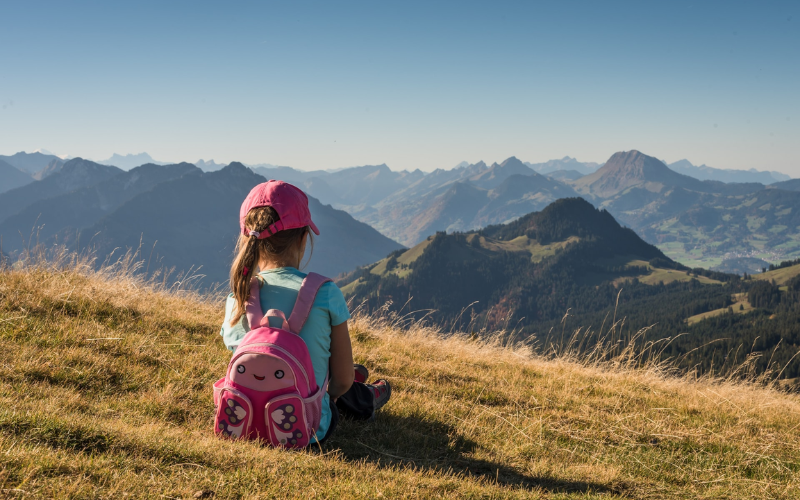 Adorable kid girl showcasing simple and cute kids hairstyle while sitting atop a mountain