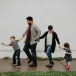 A white building serves as the backdrop for a family of four walking together, practicing gentle parenting.