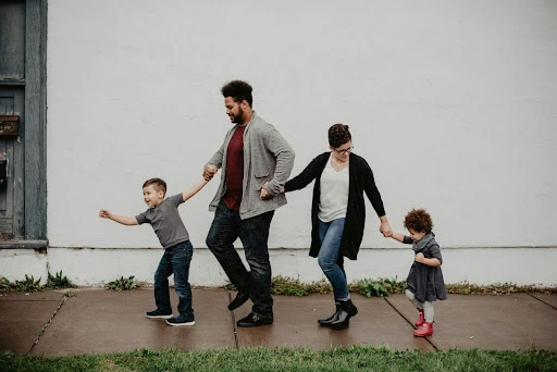 A white building serves as the backdrop for a family of four walking together, practicing gentle parenting.